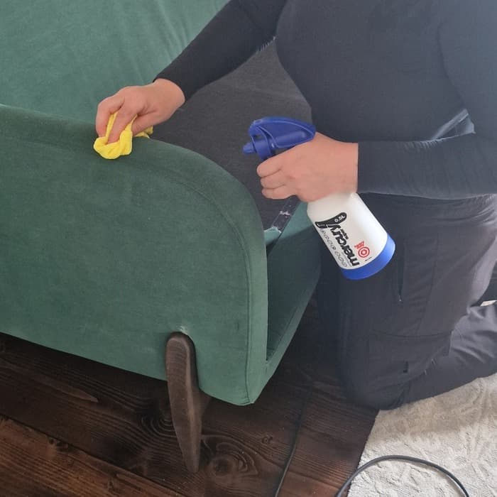 Hands carefully cleaning the fabric of a green chair